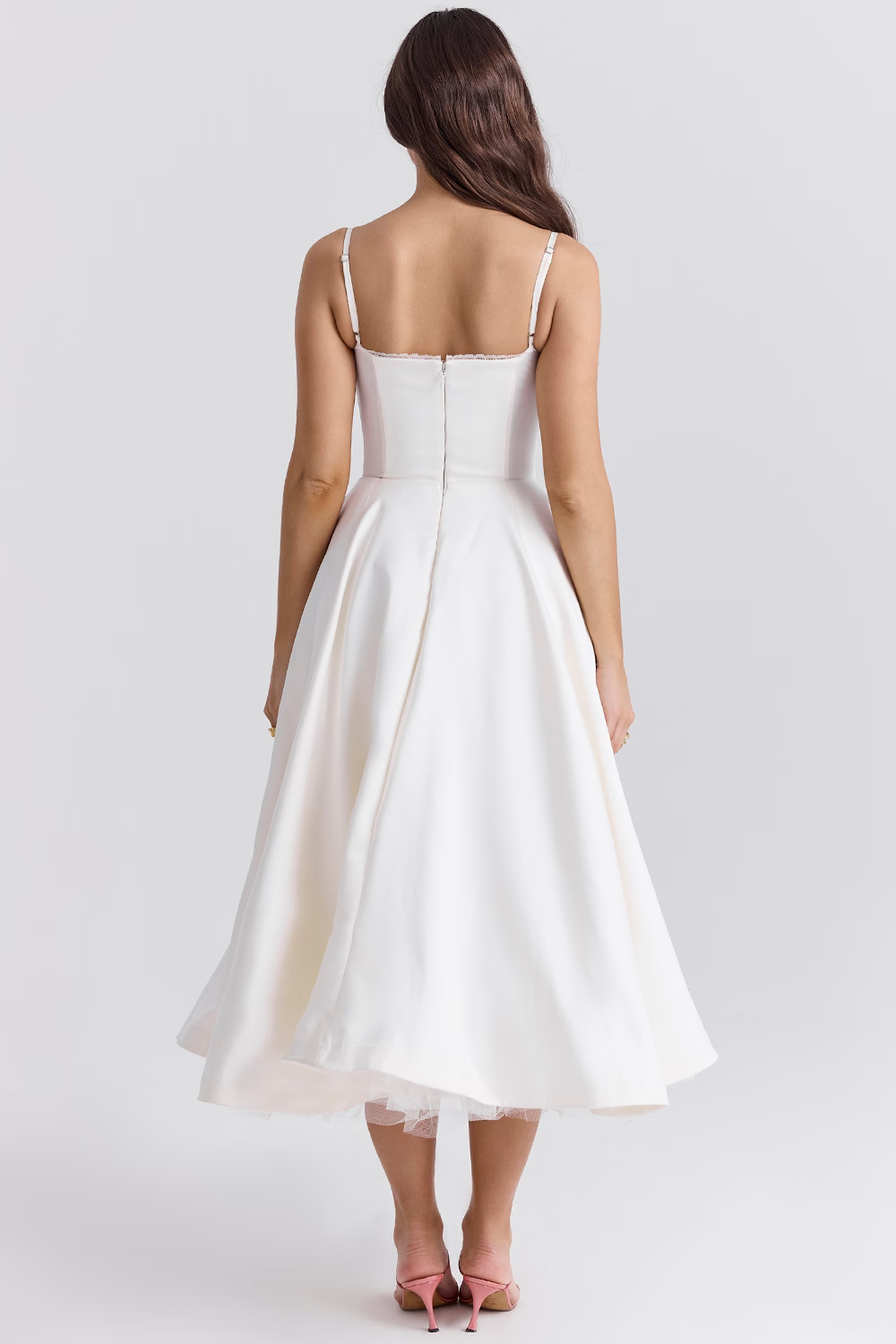 Donna in abito da sposa bianco senza spalline, vista posteriore, lunghezza media, con scarpe rosa. Elegante e moderno, perfetto per matrimoni.