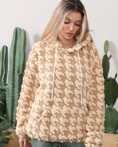 Donna con felpa beige a fantasia pied de poule, cappuccio e lacci bianchi, davanti a cactus verdi. Moda autunno inverno, abbigliamento casual.
