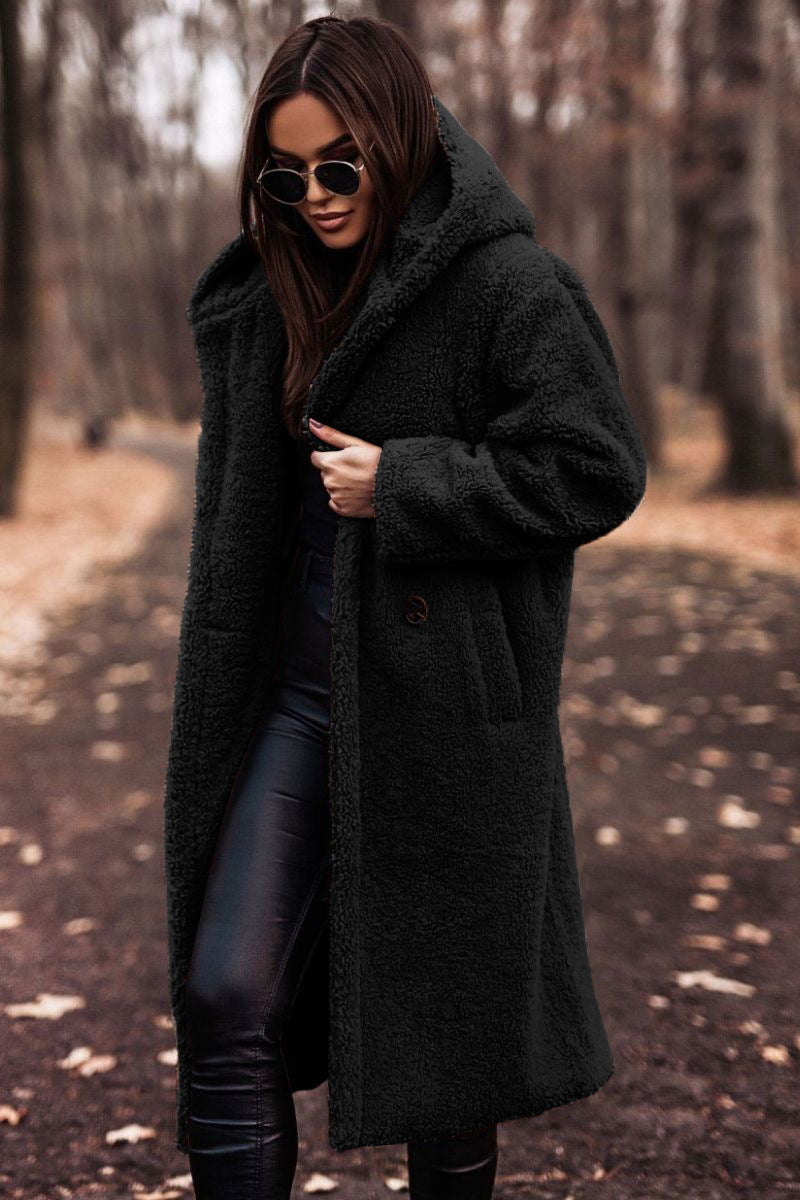 Donna con cappotto nero in pelliccia sintetica, occhiali da sole, pantaloni in pelle, cammina in un parco autunnale. Moda autunno inverno.