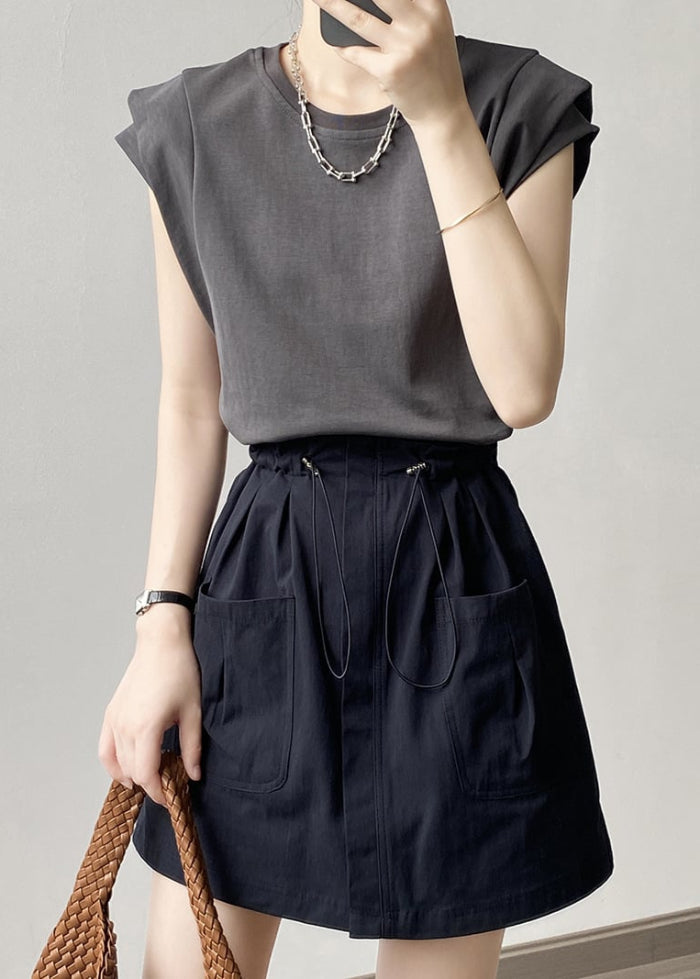 Donna con maglietta grigia e gonna nera a vita alta con tasche, indossa collana e bracciale, tiene borsa intrecciata. Moda casual elegante.