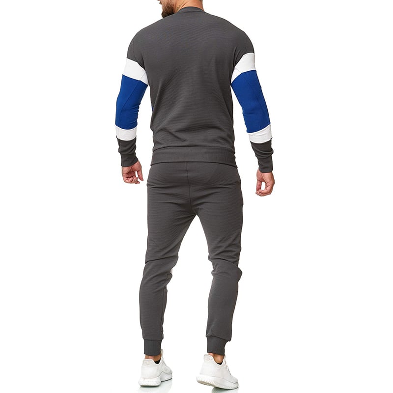 Uomo in tuta sportiva grigia con dettagli blu e bianchi, vista posteriore. Indossa scarpe da ginnastica bianche. Abbigliamento casual maschile.