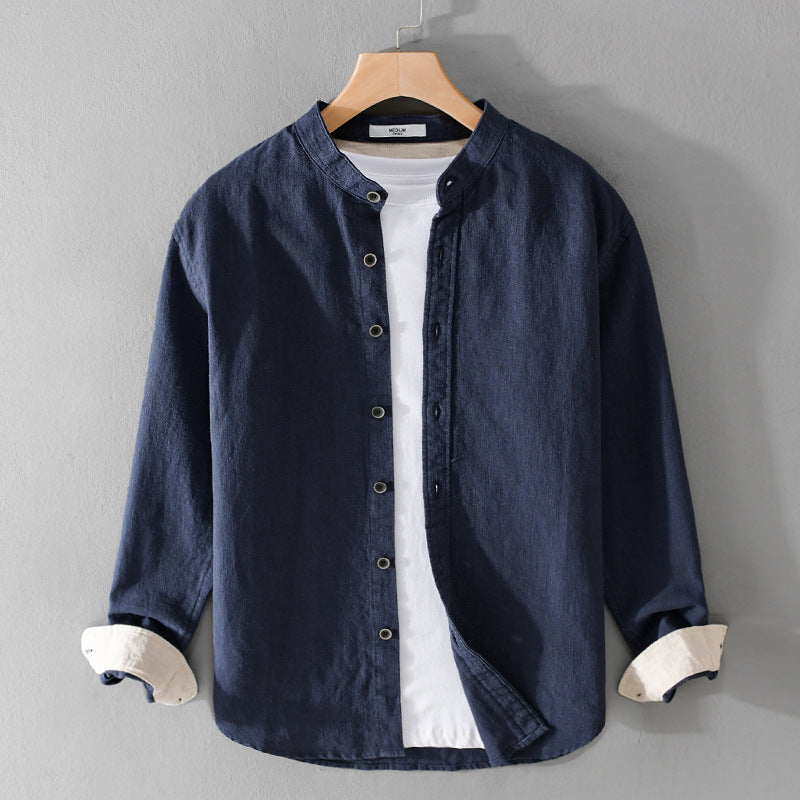 Camicia casual blu scuro da uomo con colletto alla coreana, abbinata a una t-shirt bianca, appesa su gruccia di legno. Moda maschile elegante.