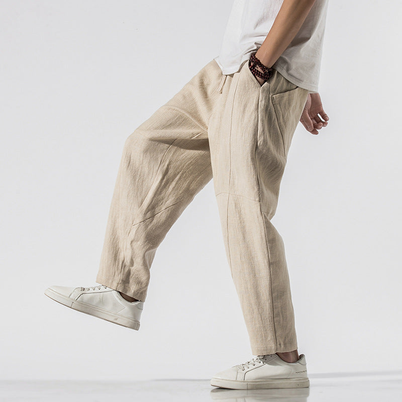 Pantaloni larghi in lino beige, indossati con scarpe da ginnastica bianche e maglietta bianca. Stile casual e confortevole per uomo.