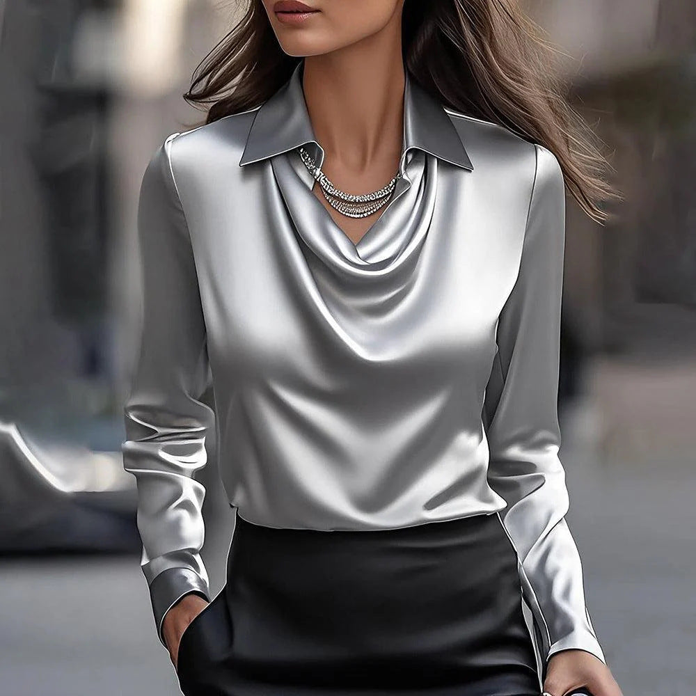 Donna con camicia di seta grigia e collana elegante, sfondo urbano sfocato. Moda femminile, abbigliamento elegante, stile sofisticato.