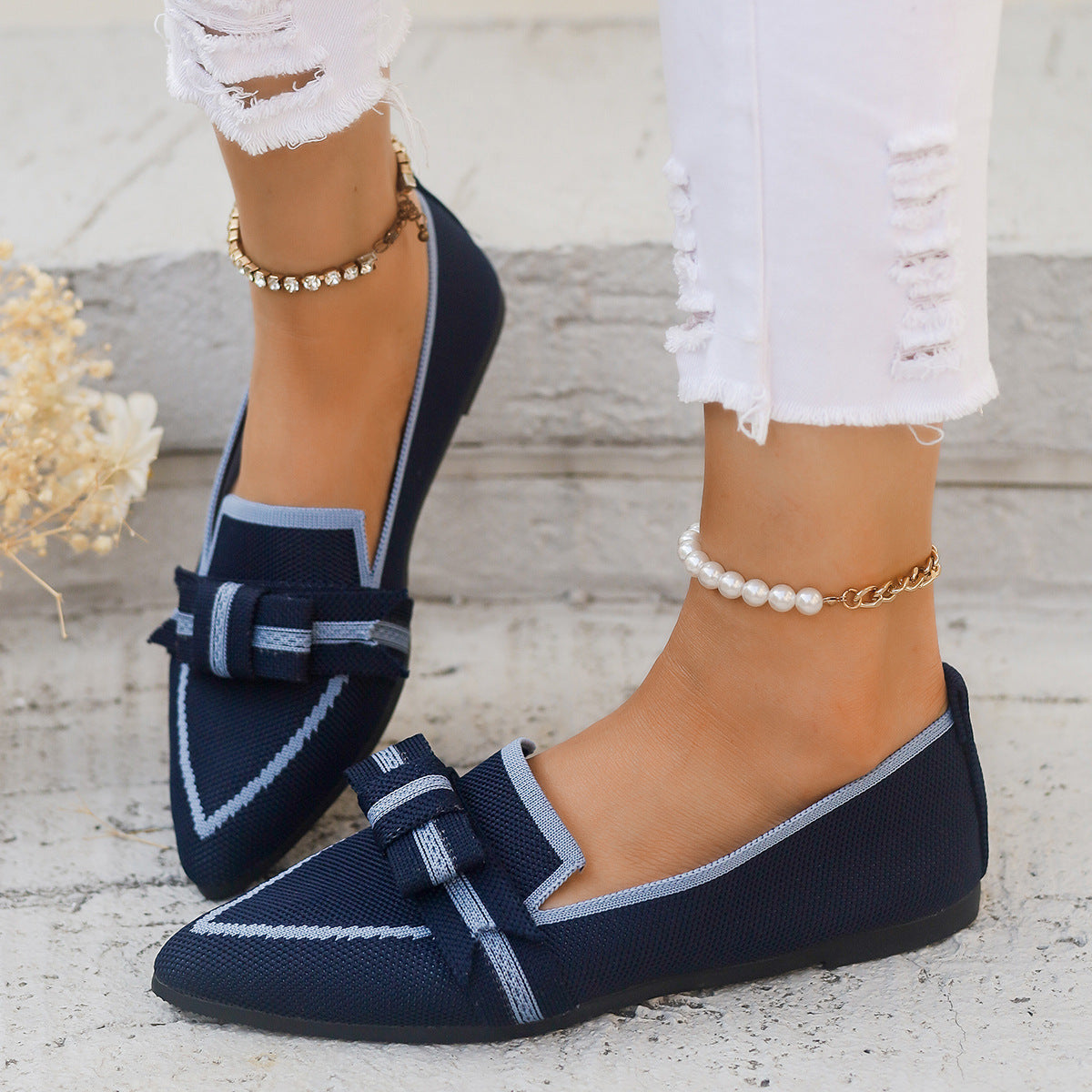 Scarpe mocassini blu scuro con fiocco, indossate con jeans bianchi strappati. Accessori: cavigliere con perle e strass. Moda casual elegante.