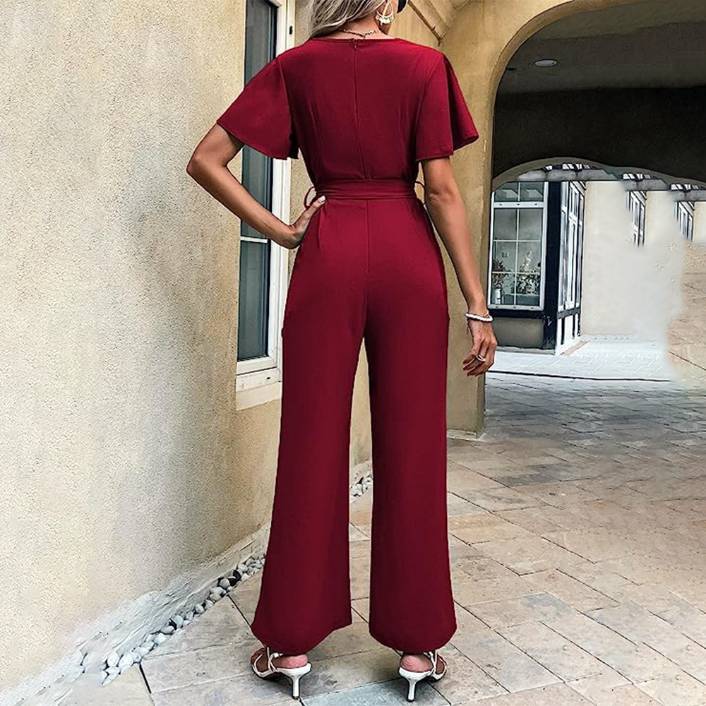 Donna in tuta rossa elegante, vista posteriore, in piedi su pavimento in pietra, vicino a edificio beige. Moda femminile, abbigliamento estivo chic.