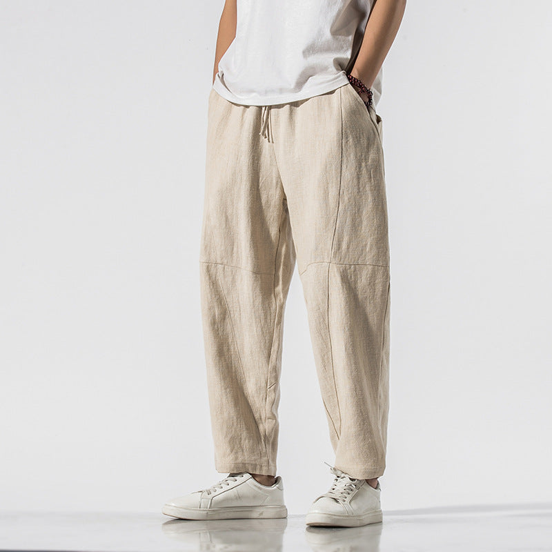 Pantaloni larghi beige in lino, stile casual, indossati con t-shirt bianca e sneakers bianche. Moda uomo, abbigliamento estivo, look rilassato.