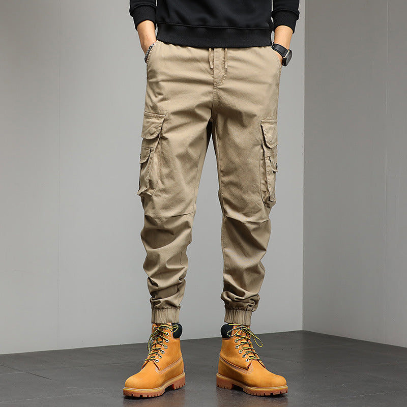 Pantaloni cargo beige da uomo con tasche laterali, abbinati a stivali gialli robusti. Moda casual maschile, abbigliamento outdoor autunnale.