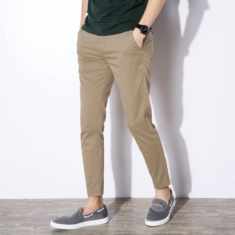 Pantaloni chino beige da uomo, abbinati a mocassini grigi e maglietta verde scuro. Stile casual elegante, moda maschile contemporanea.
