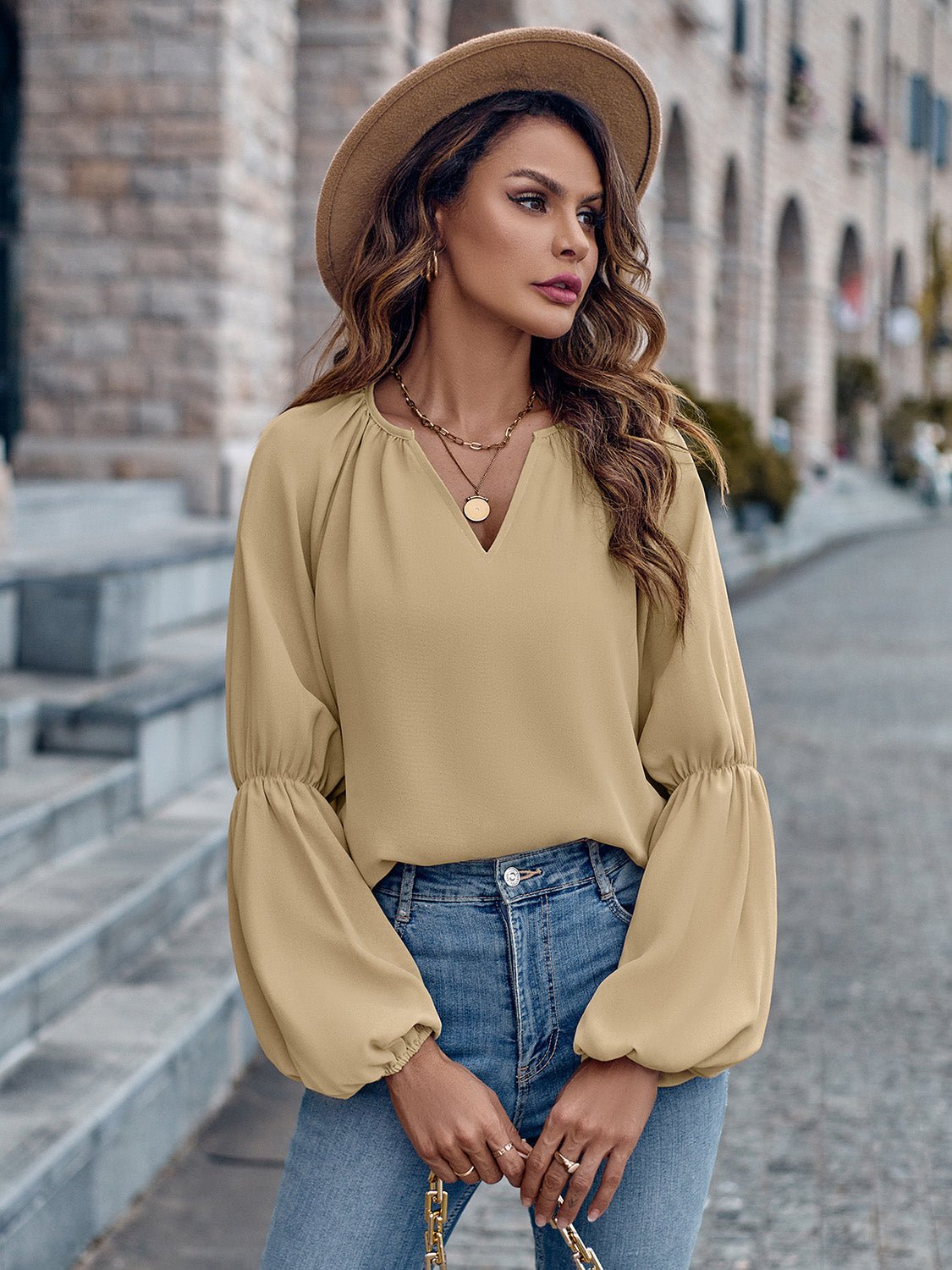 Donna con cappello beige, camicetta gialla a maniche lunghe e jeans, in posa su strada cittadina. Moda autunnale, stile casual chic.
