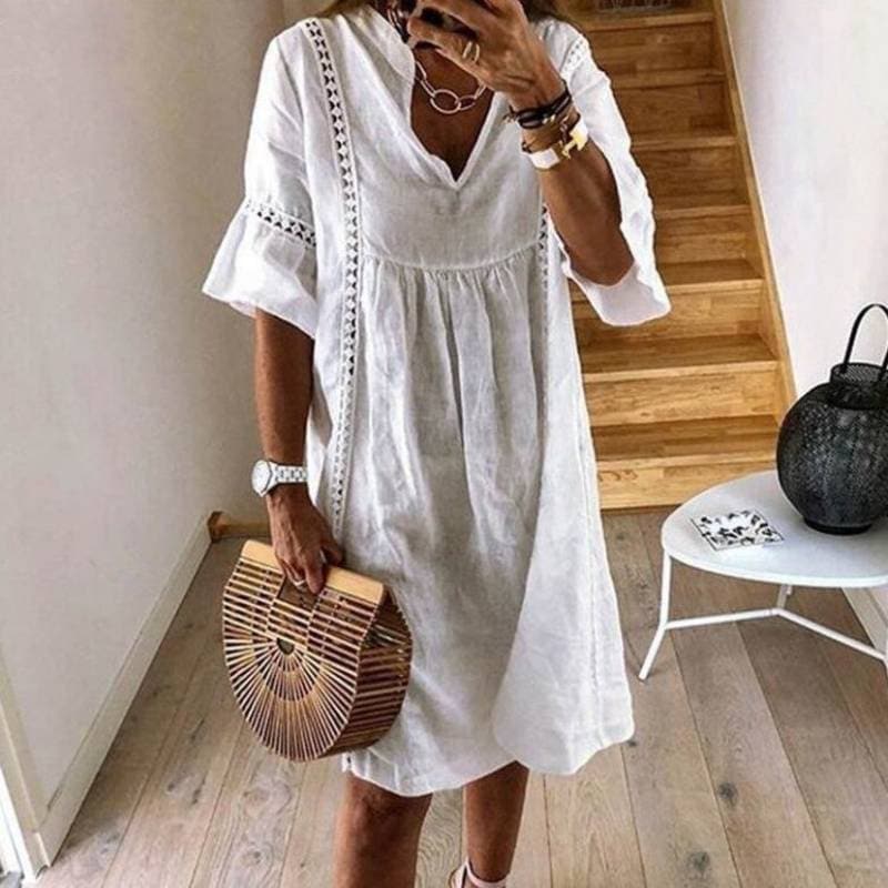 Donna con abito bianco estivo in lino, borsa di legno a semicerchio, accessori eleganti, in un ambiente moderno con scale in legno.