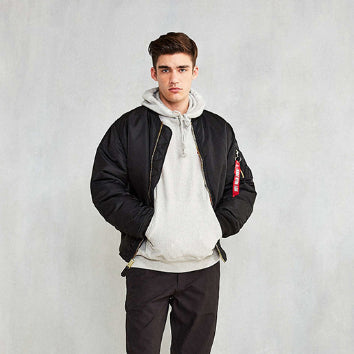 Giovane uomo con giacca bomber nera e felpa grigia con cappuccio, posa casual su sfondo neutro. Moda streetwear maschile, abbigliamento urbano.
