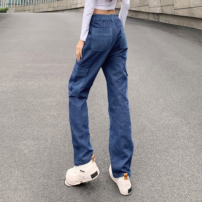 Donna in jeans cargo blu e sneakers bianche su strada asfaltata. Moda casual, pantaloni larghi, stile urbano.