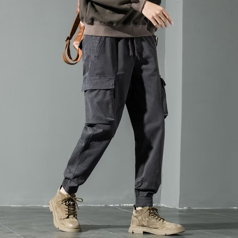 Pantaloni cargo neri da uomo, tasche laterali, stile casual, abbinati a scarpe beige e felpa marrone. Moda urbana, abbigliamento maschile trendy.