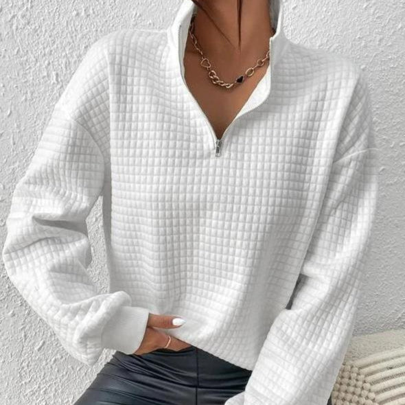 Maglione bianco trapuntato con zip, indossato da una persona, abbinato a pantaloni in pelle nera e collana a catena. Moda autunnale elegante.