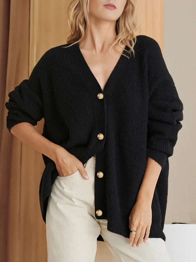 Donna indossa cardigan nero oversize con bottoni dorati, abbinato a pantaloni chiari. Moda autunnale elegante e casual.
