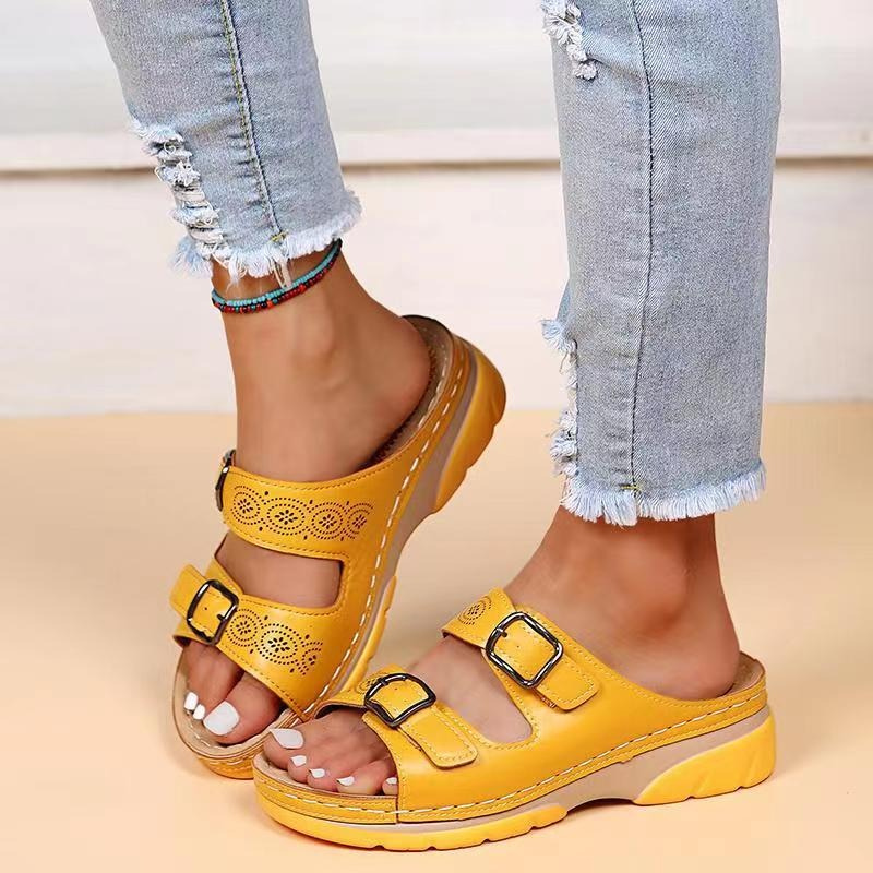 Sandali gialli con doppia fibbia su piedi femminili, abbinati a jeans strappati. Calzature estive comode, moda casual donna.
