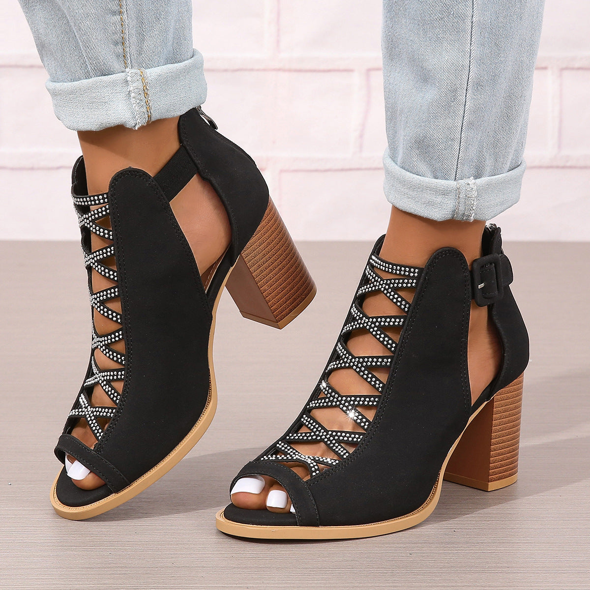 Sandali neri con tacco alto e cinturino, design traforato e dettagli con strass, indossati con jeans chiari. Scarpe eleganti da donna.