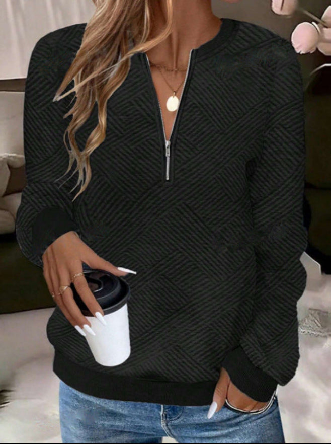 Donna con maglione nero a motivi geometrici, jeans, collana dorata, tiene una tazza da caffè. Stile casual, moda autunnale, comfort quotidiano.