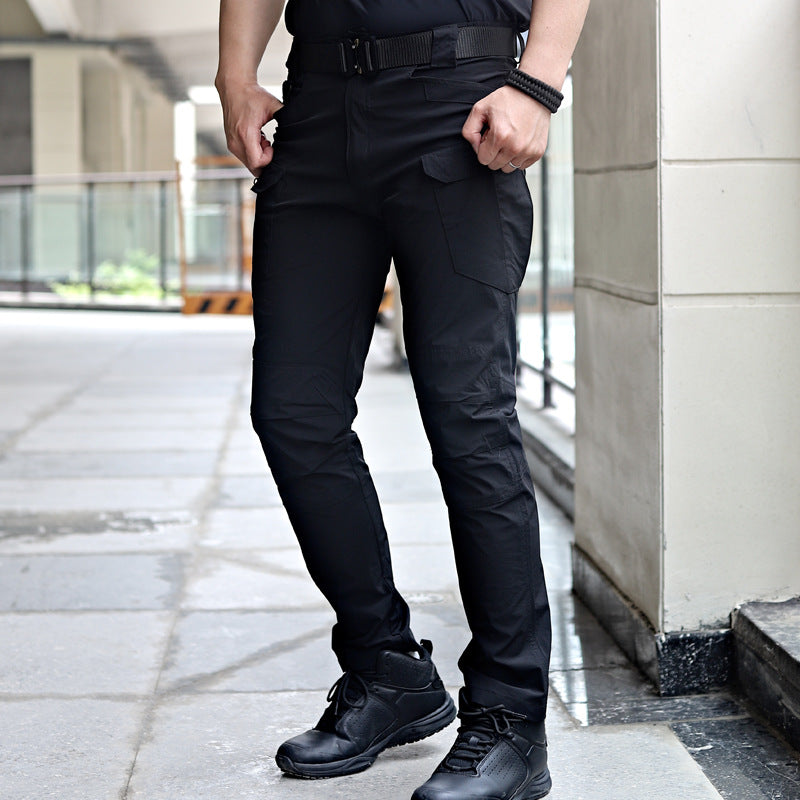Uomo in pantaloni tattici neri, scarpe da trekking, posa urbana. Abbigliamento outdoor resistente, moda funzionale, stile casual moderno.