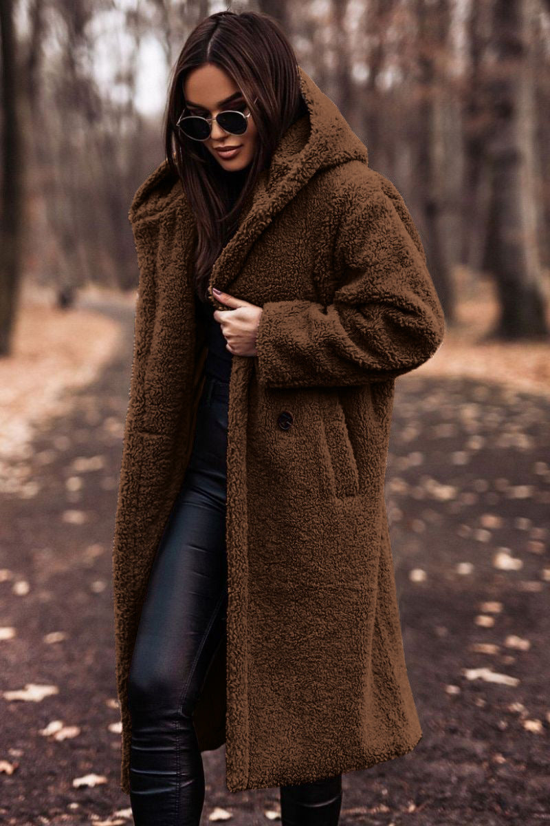 Donna con cappotto teddy marrone, occhiali da sole neri, pantaloni in pelle nera, in un parco autunnale. Moda autunno inverno, stile casual chic.