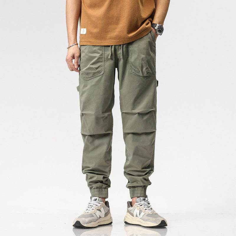 Pantaloni cargo verde oliva da uomo, tasche multiple, stile casual, abbinati a scarpe da ginnastica bianche e maglietta marrone.