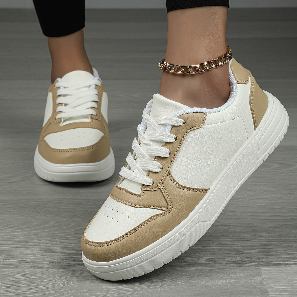 Scarpe da ginnastica bianche e beige su pavimento in legno, indossate con cavigliera dorata. Design moderno, casual e alla moda.