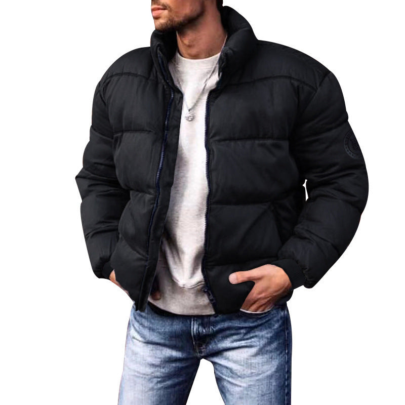 Giacca invernale uomo nera imbottita, stile casual, con zip frontale e colletto alto, indossata su maglia grigia e jeans. Moda maschile autunno inverno.