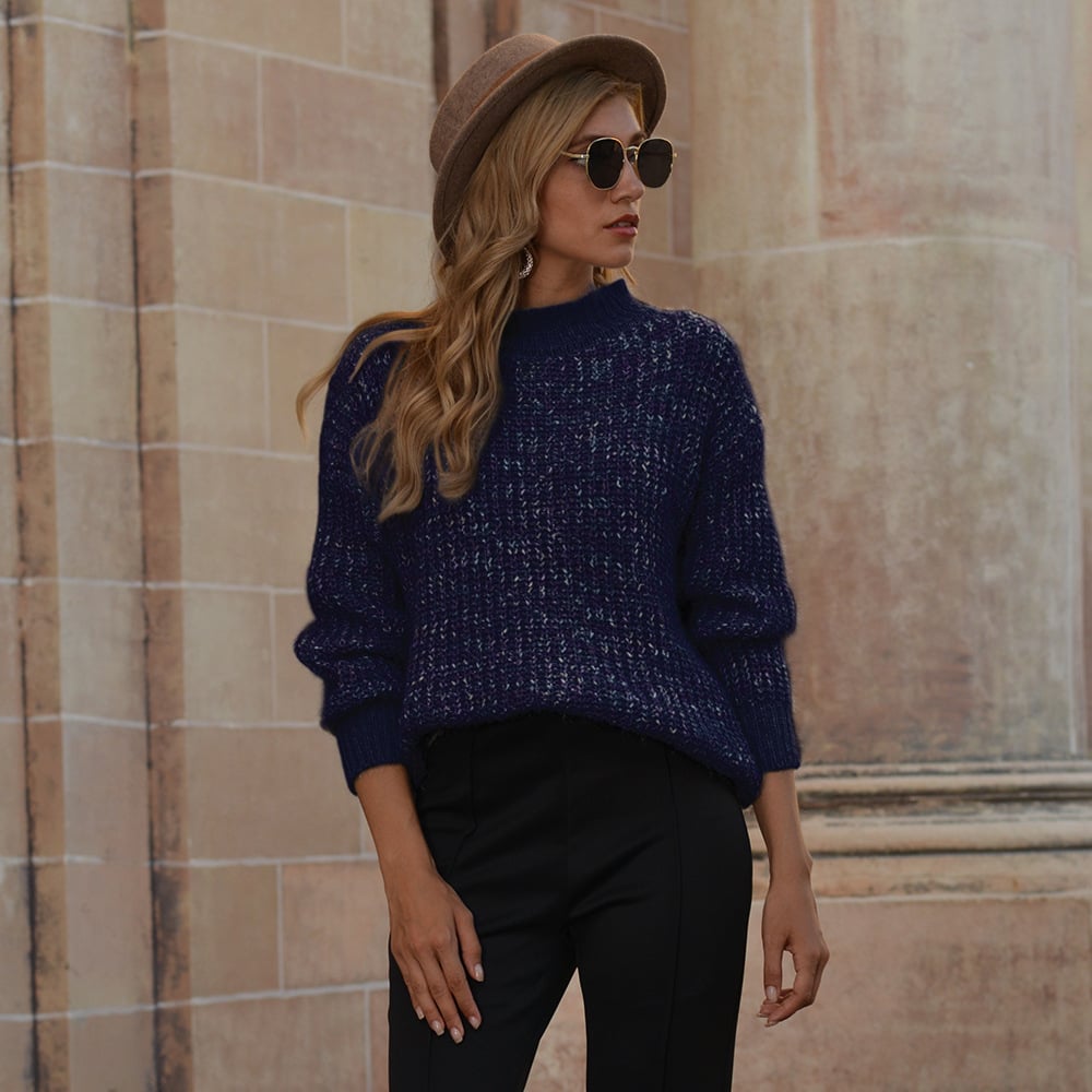 Donna con cappello marrone, occhiali da sole e maglione blu, posa davanti a un edificio storico. Moda autunnale, stile urbano elegante.