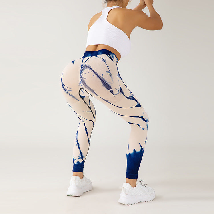Donna in abbigliamento sportivo, leggings tie-dye blu e bianchi, top bianco, scarpe da ginnastica bianche, posa fitness su sfondo neutro.