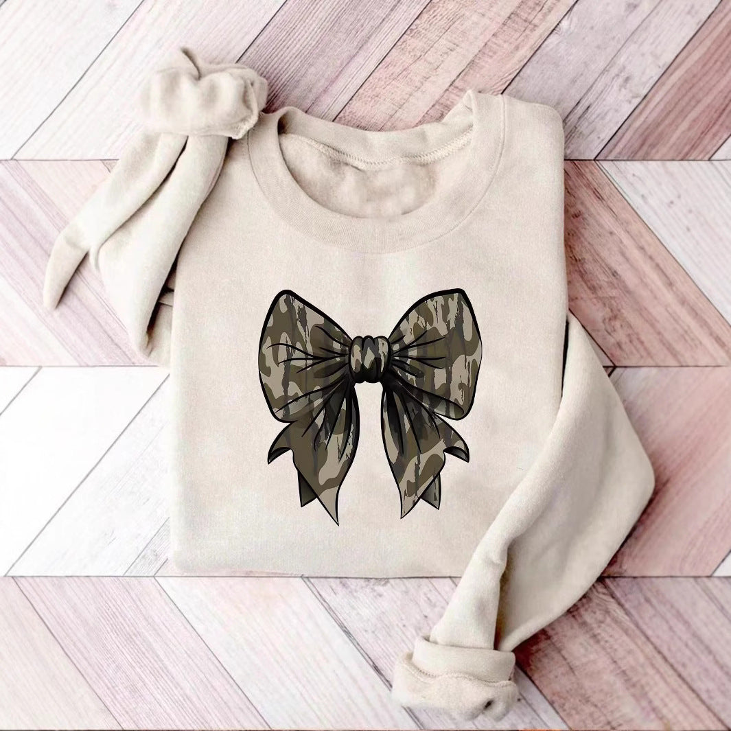 Felpa beige con fiocco stampato in stile mimetico su pavimento in legno chiaro. Moda casual, abbigliamento autunnale, design trendy.