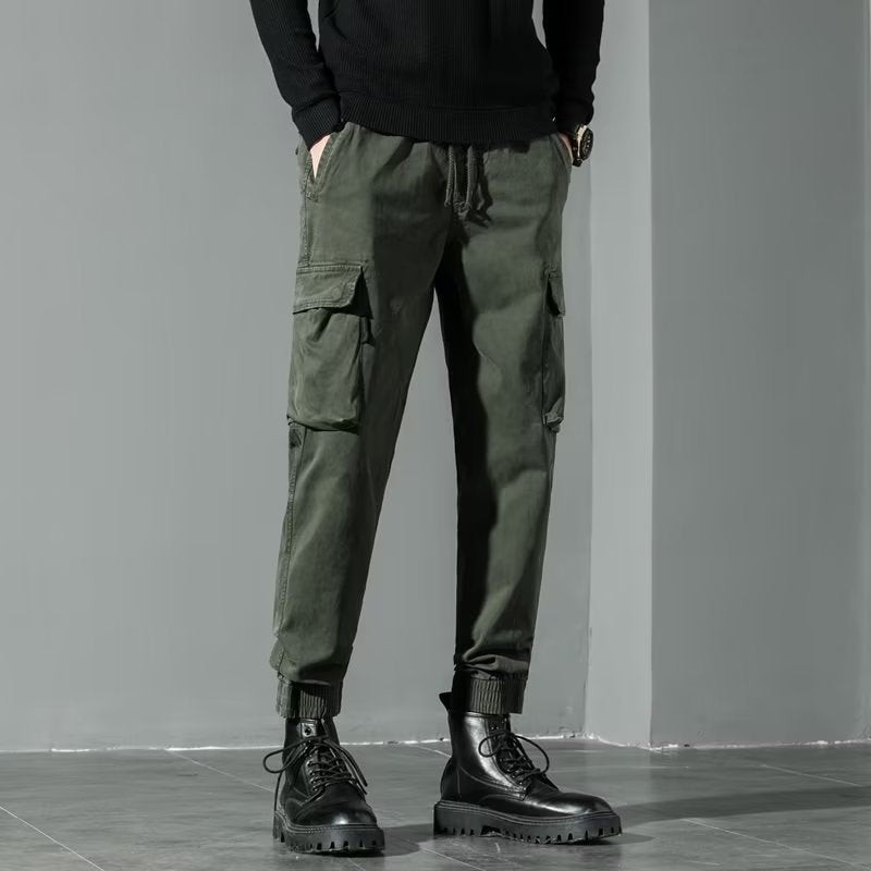 Pantaloni cargo verde militare da uomo, tasche multiple, abbinati a stivali neri robusti. Stile casual e funzionale per moda urbana.