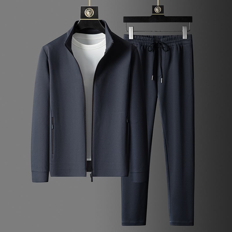 Completo sportivo uomo blu scuro, giacca con zip e pantaloni con coulisse, su sfondo grigio. Abbigliamento casual elegante e moderno.