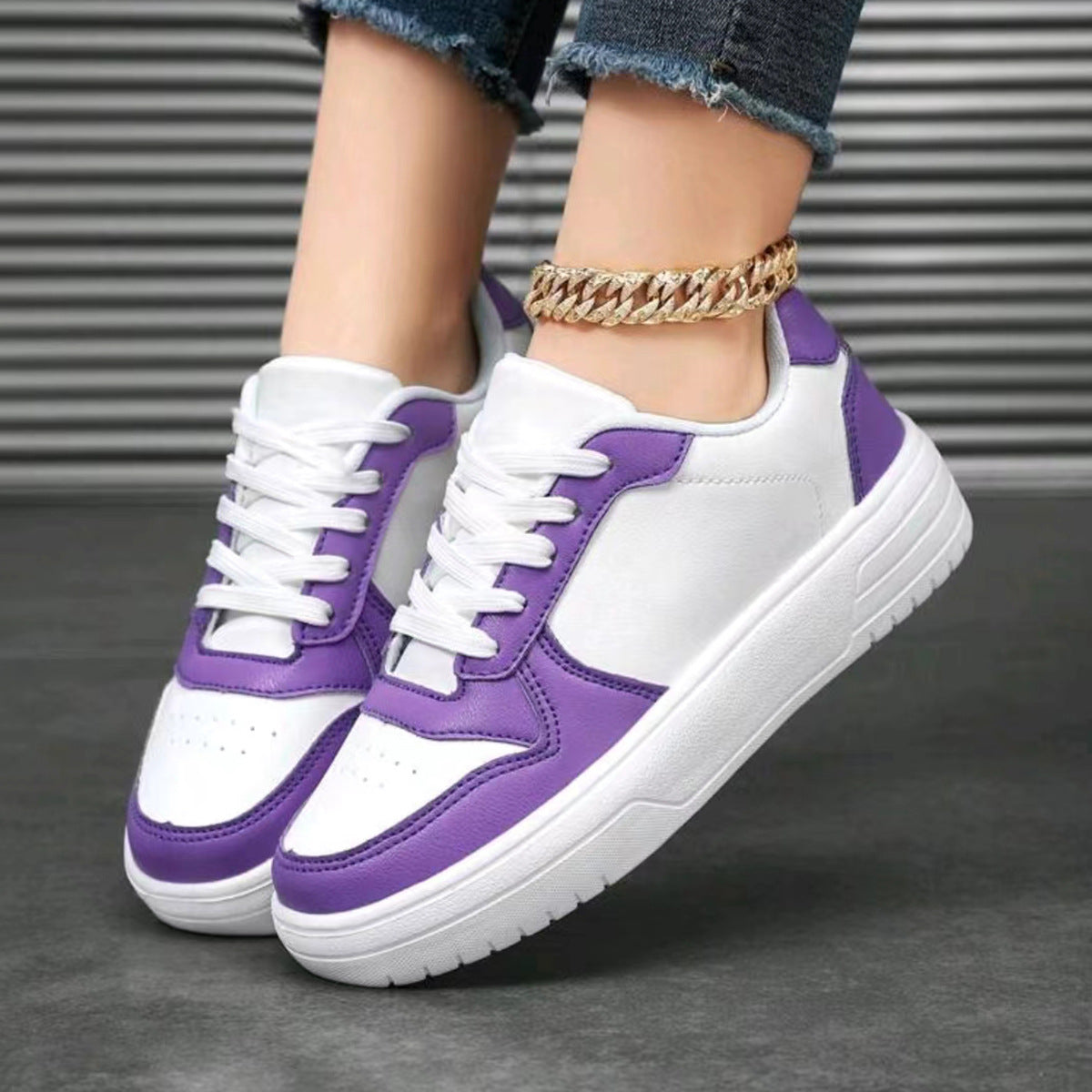Scarpe da ginnastica bianche e viola su sfondo grigio, indossate con jeans strappati e cavigliera dorata. Sneakers moda donna, stile casual.