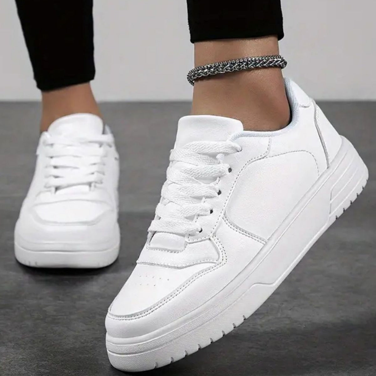 Scarpe da ginnastica bianche su pavimento grigio, indossate con pantaloni neri. Design moderno, suola spessa, perfette per moda casual e sportiva.