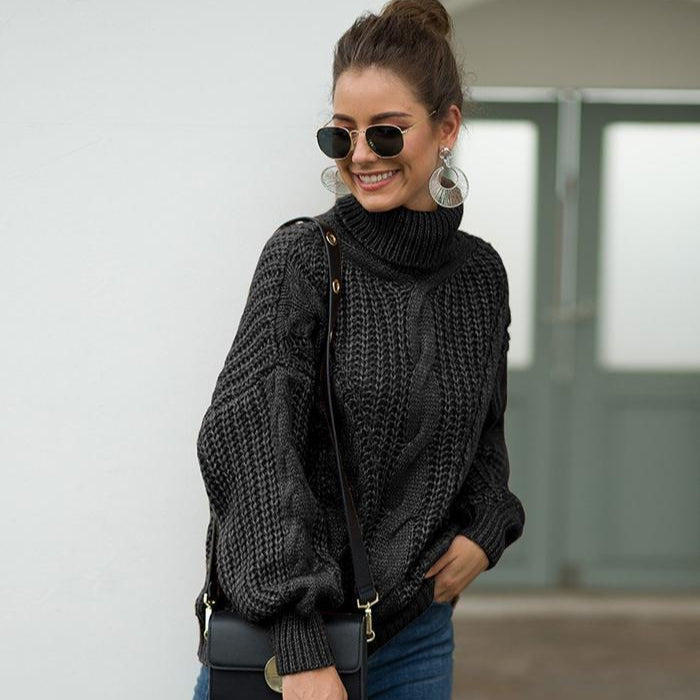 Donna con occhiali da sole indossa maglione nero a collo alto, orecchini grandi e borsa a tracolla. Moda autunnale, stile casual chic.