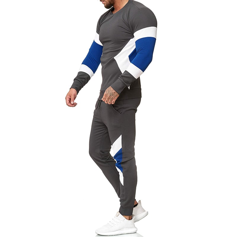 Uomo in tuta sportiva grigia con dettagli blu e bianchi, scarpe da ginnastica bianche. Abbigliamento casual per fitness e tempo libero.