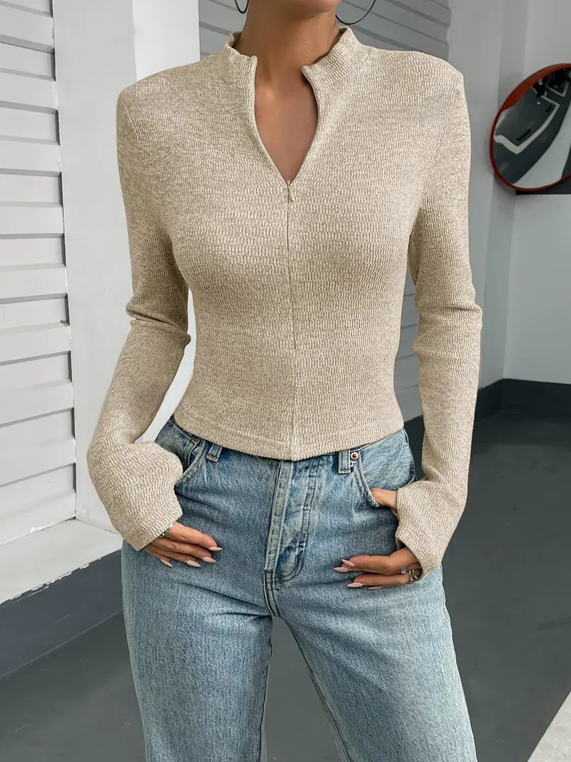 Donna con maglione beige a maniche lunghe e jeans a vita alta, posa casualmente. Moda autunnale, abbigliamento casual chic, tendenze femminili.