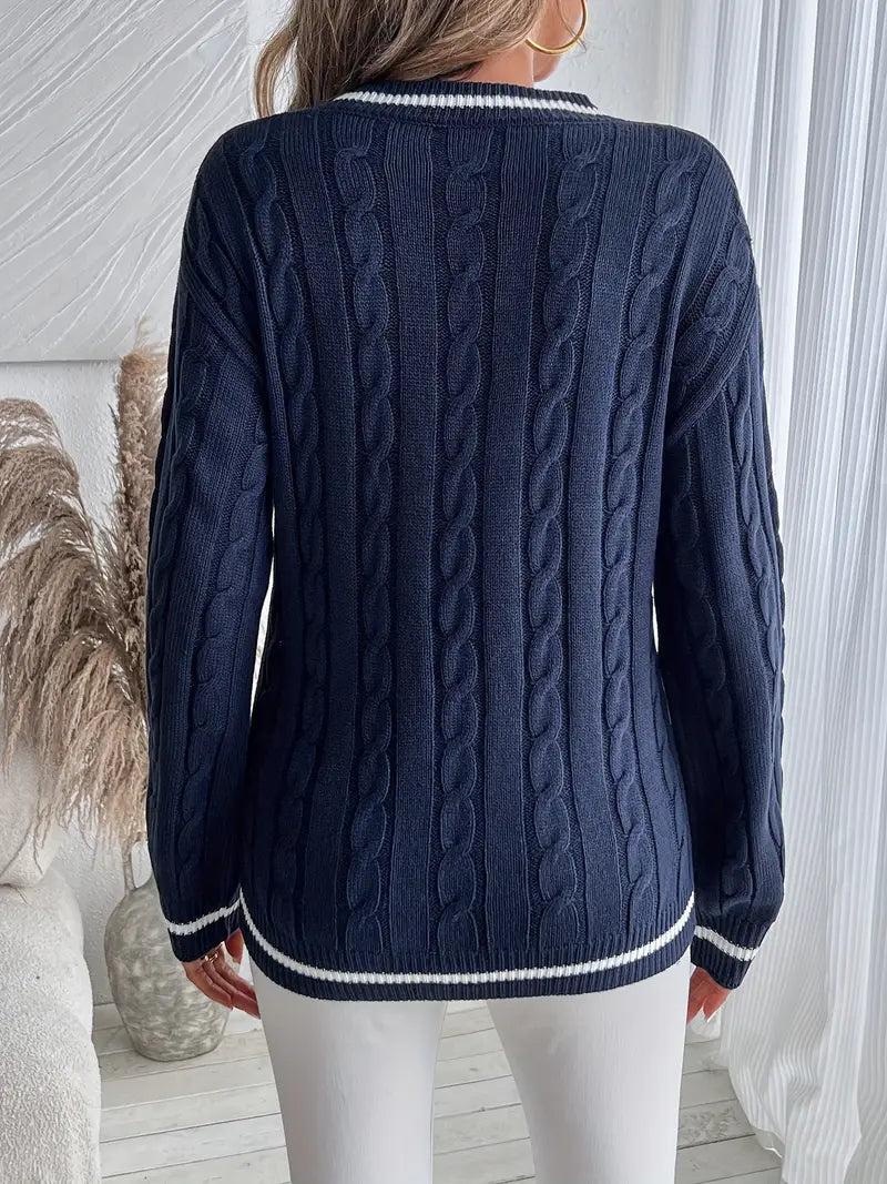 Maglione blu navy a trecce, maniche lunghe, indossato da una persona di spalle, ambientato in un interno moderno con decorazioni naturali.