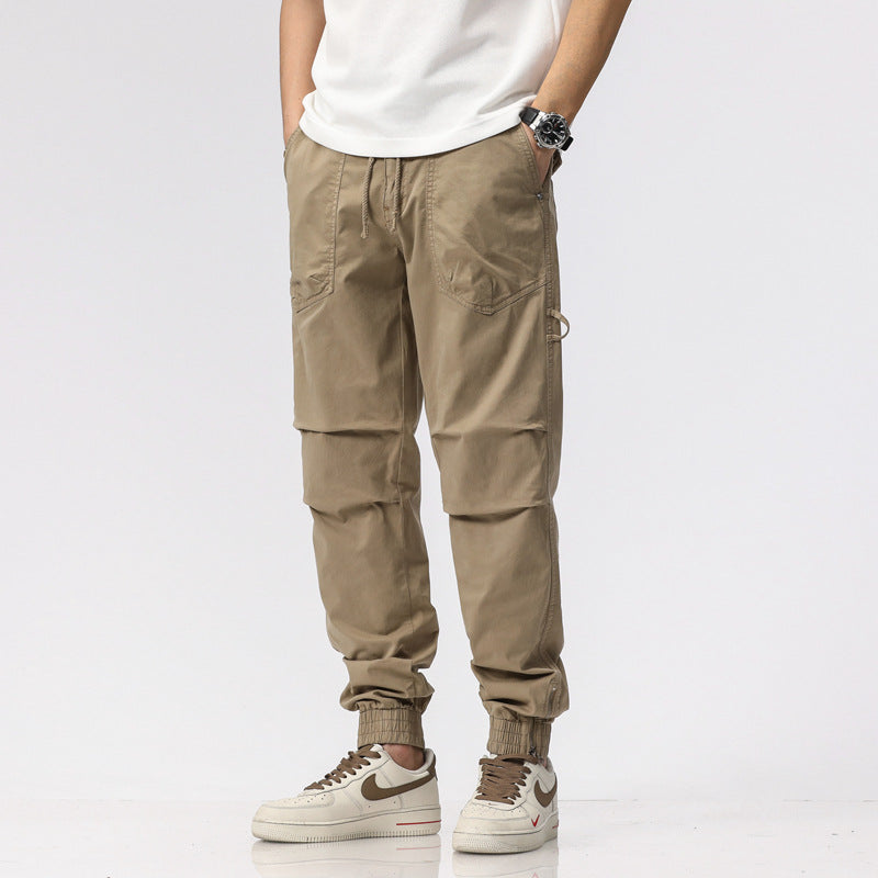 Pantaloni cargo beige da uomo, stile casual, con tasche multiple, indossati con sneakers bianche e maglietta bianca. Moda maschile contemporanea.