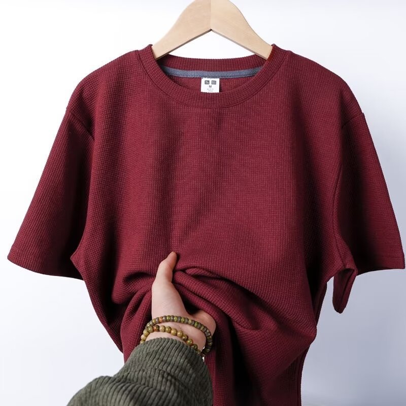 Maglietta rossa a maniche corte su appendiabiti, tessuto a coste, mano che tocca il tessuto. Abbigliamento casual, moda uomo, stile estivo.