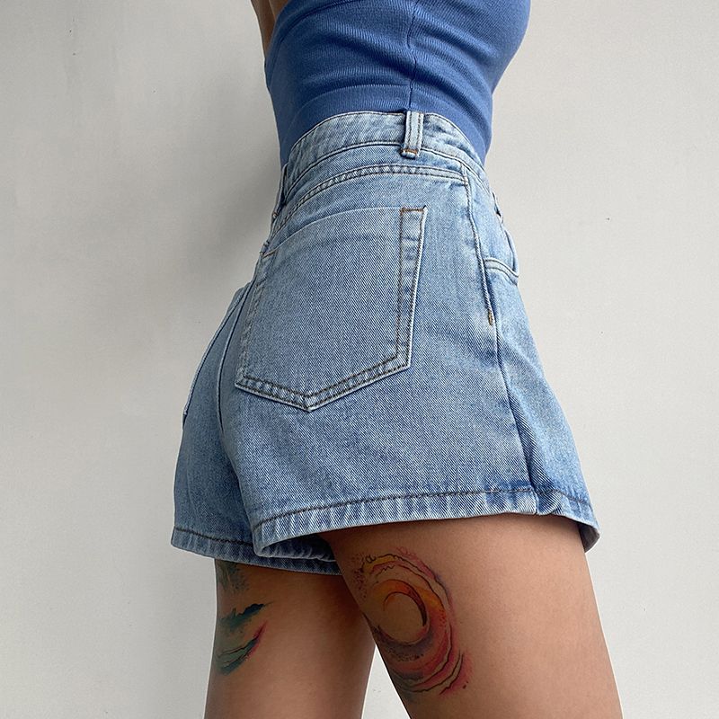 Donna in pantaloncini di jeans chiari e top blu, con tatuaggi colorati sulla coscia. Moda estiva casual, abbigliamento denim, stile urbano.