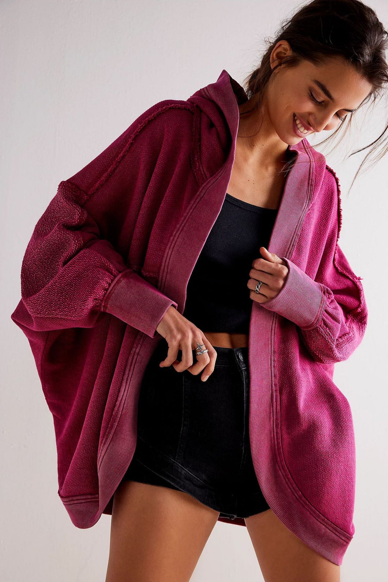 Donna sorridente indossa felpa oversize fucsia, top nero e shorts. Moda casual, abbigliamento comodo, stile autunnale.
