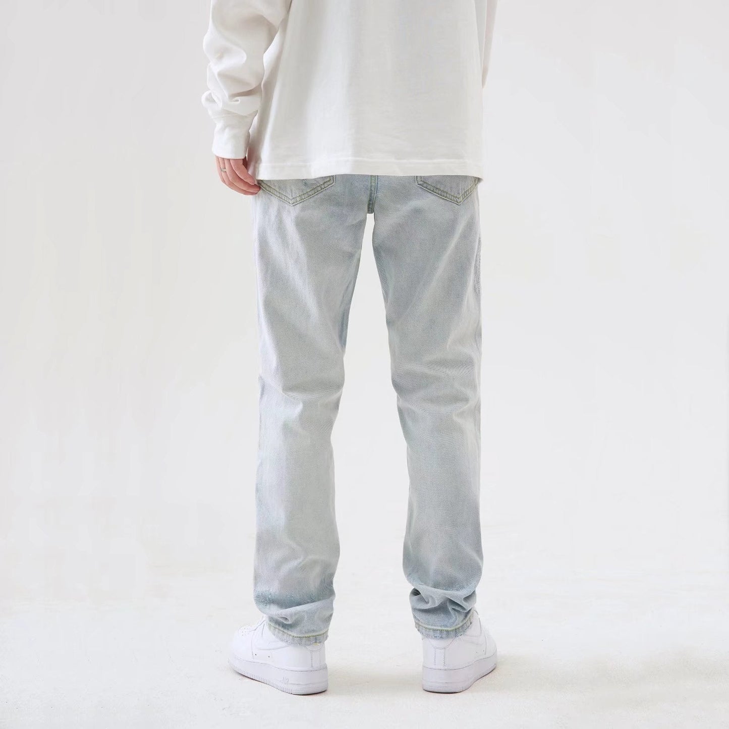 Jeans uomo chiari, vestibilità rilassata, indossati con scarpe bianche e maglia bianca. Moda casual, abbigliamento maschile trendy.