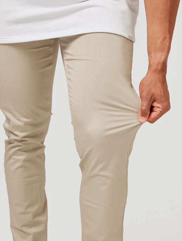 Pantaloni beige elasticizzati, uomo tira tessuto per mostrare flessibilità. Moda maschile, abbigliamento casual, comfort quotidiano.