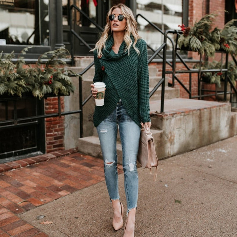 Donna con maglione verde e jeans strappati, cammina con caffè in mano. Moda autunnale, occhiali da sole, borsa beige. Sfondo urbano con decorazioni natalizie.