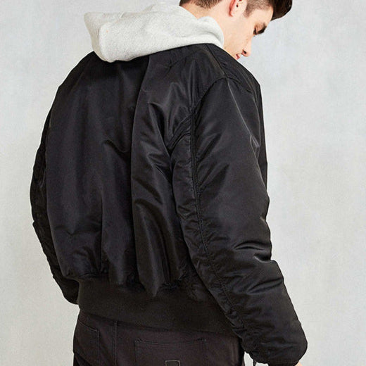 Giacca bomber nera uomo, tessuto lucido, indossata sopra felpa grigia con cappuccio. Moda casual, abbigliamento autunnale, stile urbano.