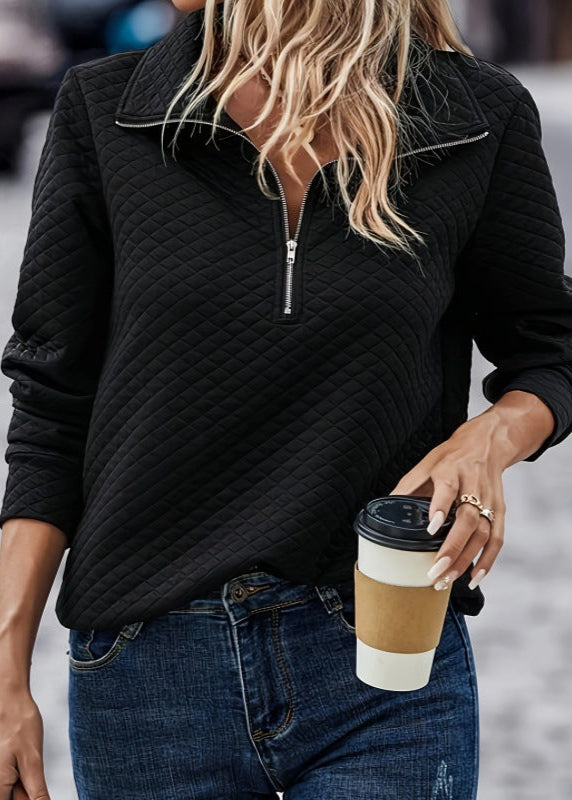 Donna con maglione nero trapuntato e jeans, tiene un caffè da asporto. Moda casual autunnale, look urbano, stile quotidiano.