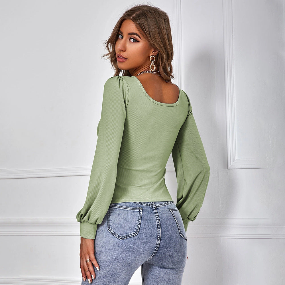 Donna con maglia verde a maniche lunghe e jeans aderenti, posa di profilo in interni eleganti. Moda femminile, abbigliamento casual chic.