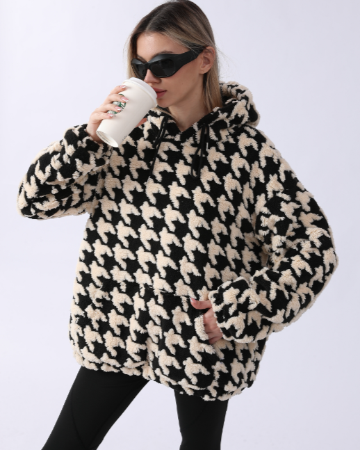 Donna con occhiali da sole indossa felpa con cappuccio a pied de poule bianco e nero, beve caffè da bicchiere di carta. Moda autunnale casual.
